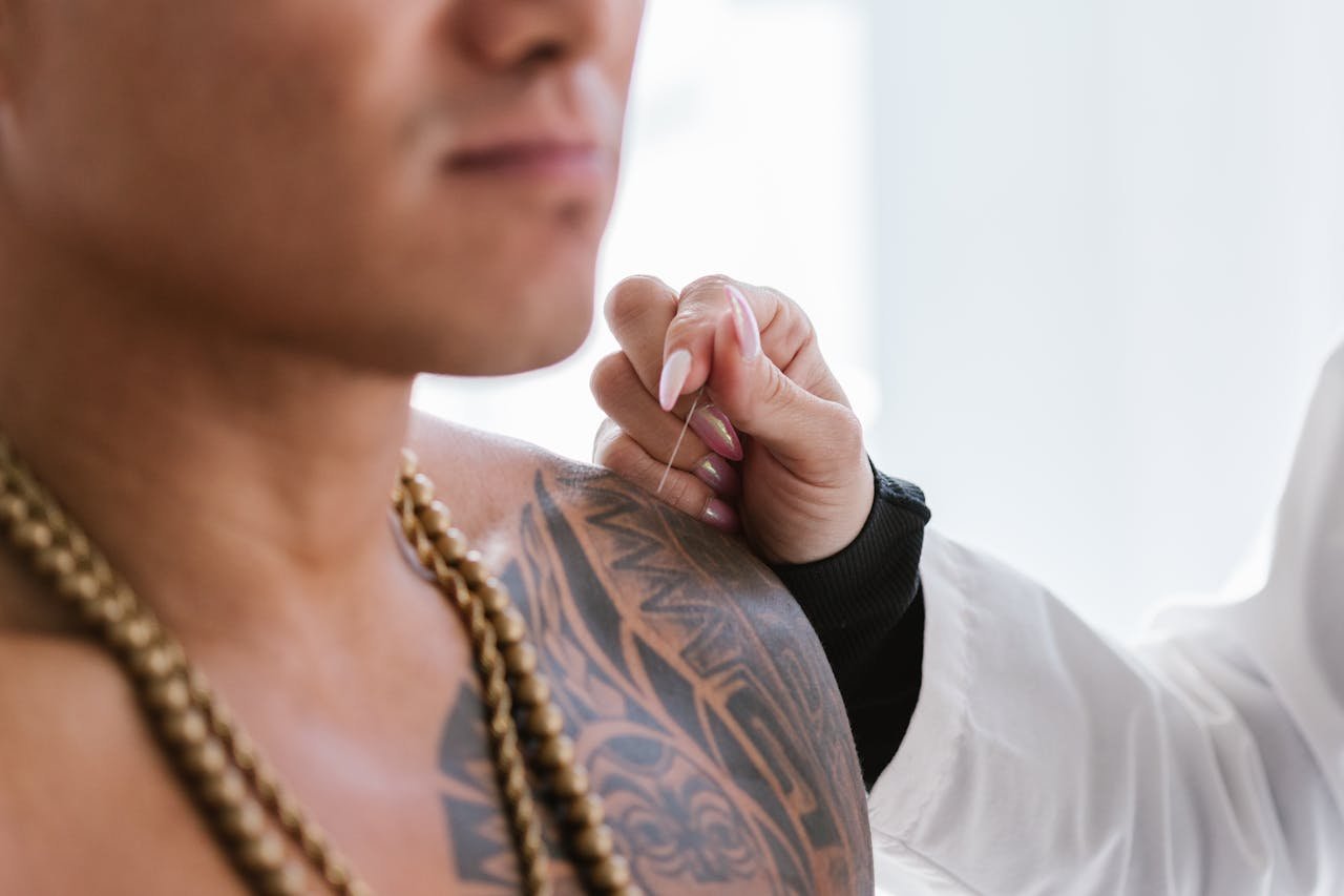 Close-up of tattooed mans shoulder, receiving acupuncture treatment by a practitioner.